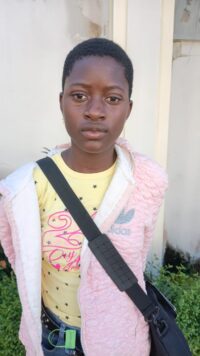 Nzerem Blessing Kamsiriyochukwu, JSS 3 student, standing outdoors in a pink jacket near a wall at the NITDA bootcamp in Enugu